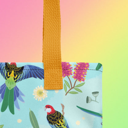 Close up of a tote bag with yellow handles and an eastern rosella parrot pattern on a gradient pink, yellow and green background