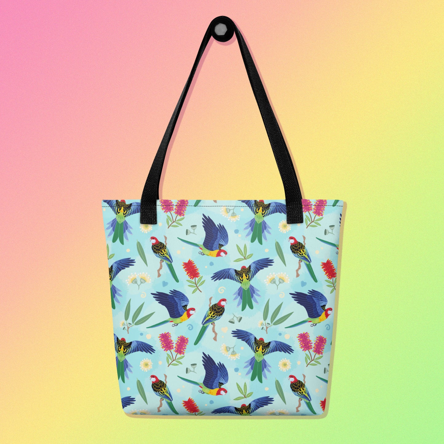 Tote bag with black handles and an eastern rosella parrot pattern on a gradient pink, yellow and green background
