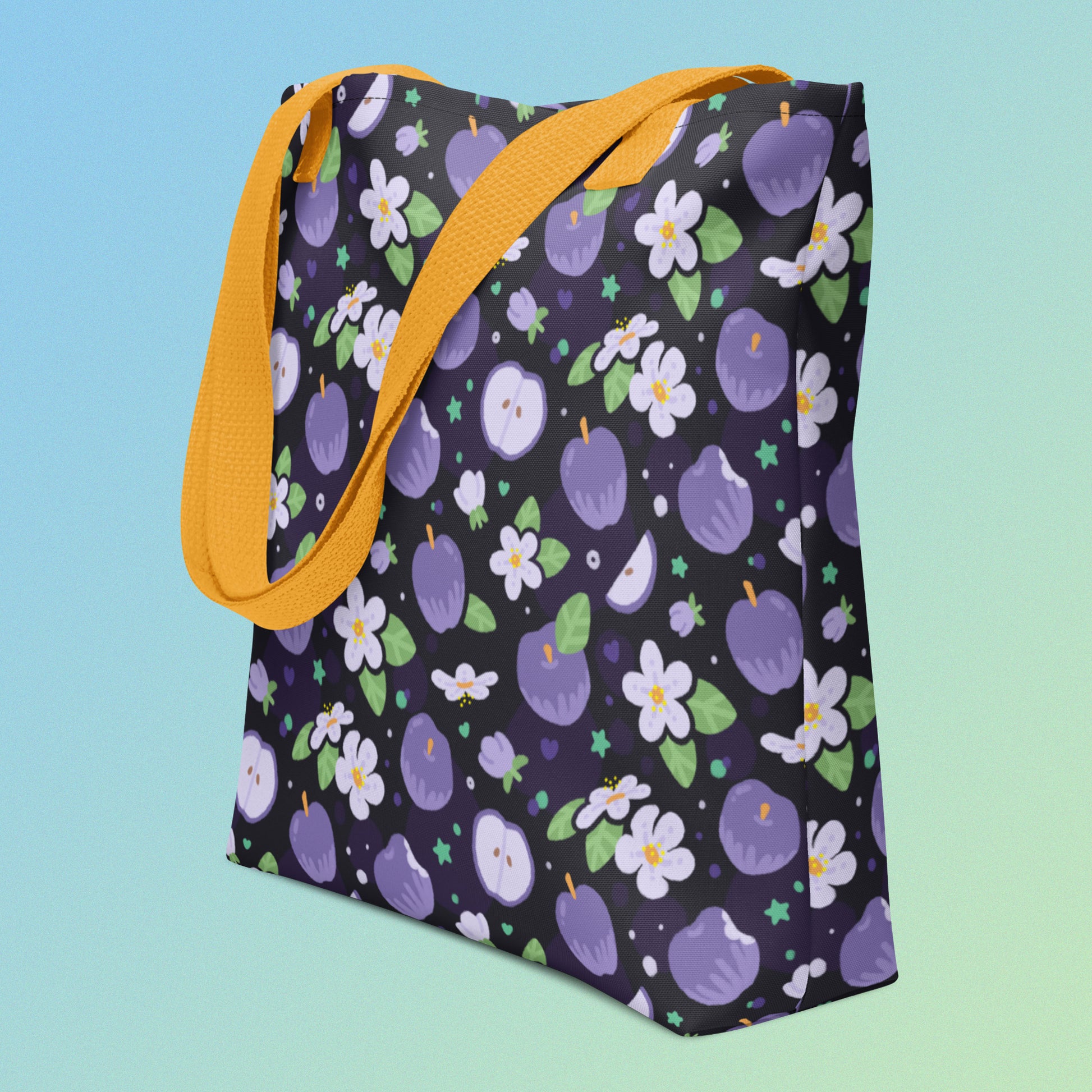 Tote bag with a yellow strap and a purple apple and flower pattern on an angle on a gradient blue and green background