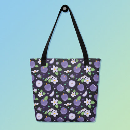 Tote bag with a black strap and purple apple and flower pattern on a gradient blue and green background