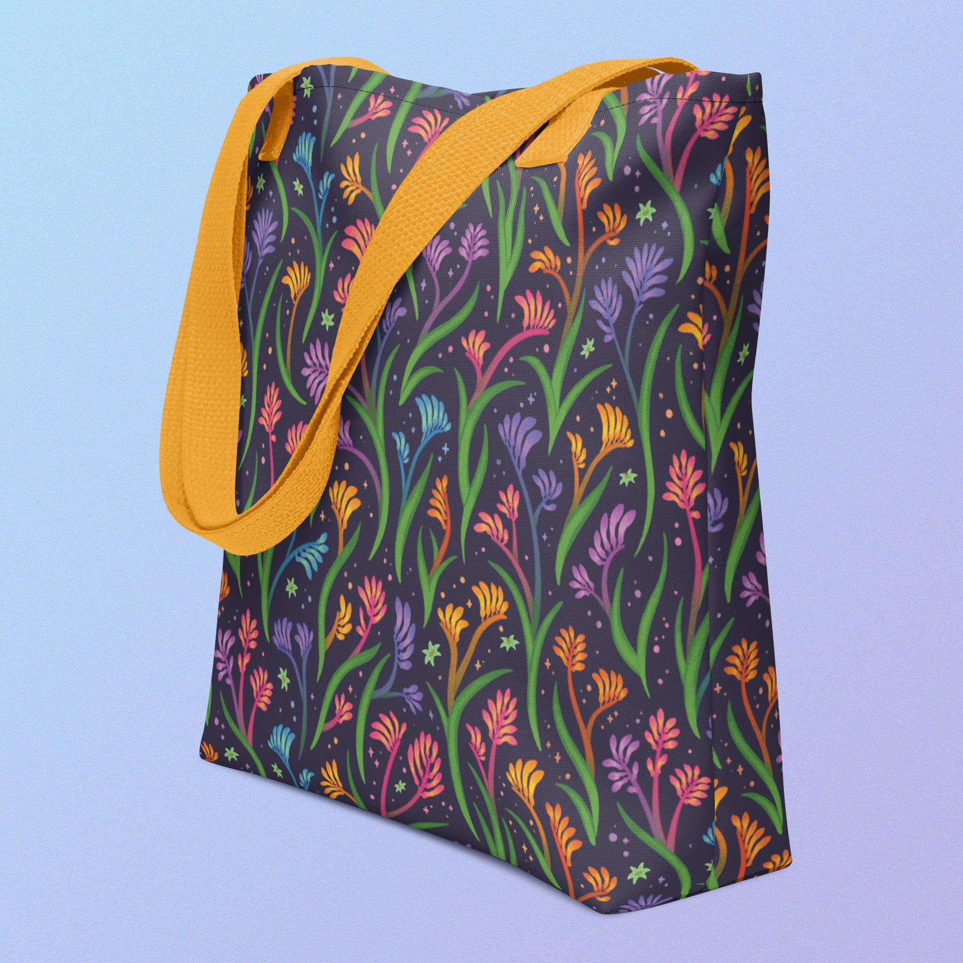 Tote bag on an angle with a yellow strap and a floral rainbow kangaroo paw pattern on a gradient blue and purple background.