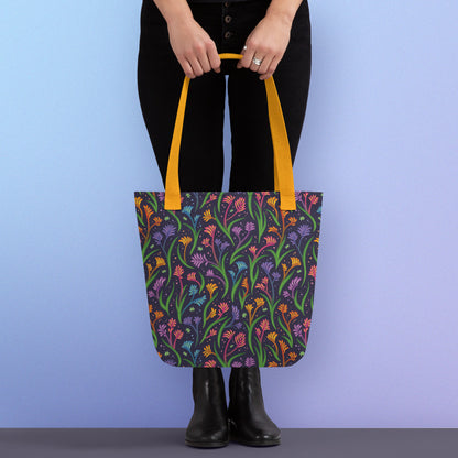 Person holding a tote bag with a yellow strap and a floral rainbow kangaroo paw pattern on a gradient blue and purple background.
