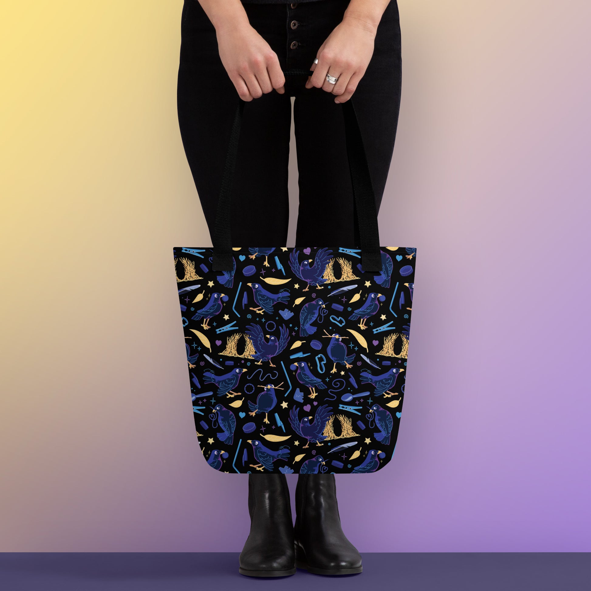 Person holding a tote bag with black handles and a black/blue/yellow satin bowerbird pattern pattern on a yellow and purple gradient background