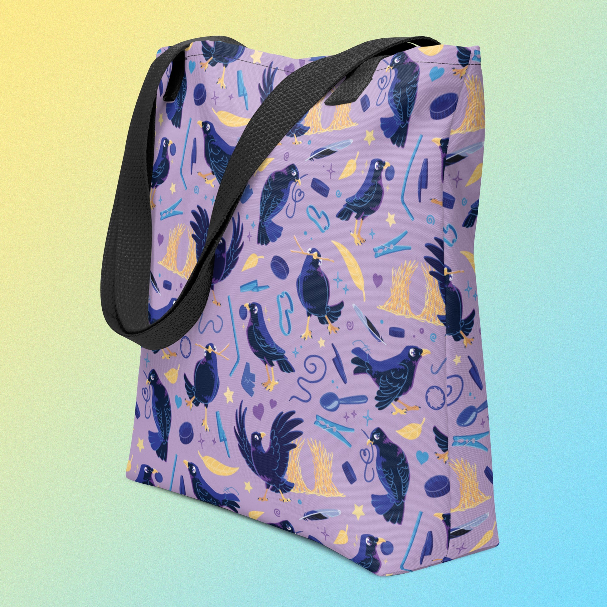 Tote bag with black handles and a purple/blue/yellow satin bowerbird pattern on an angle on a yellow and blue gradient background