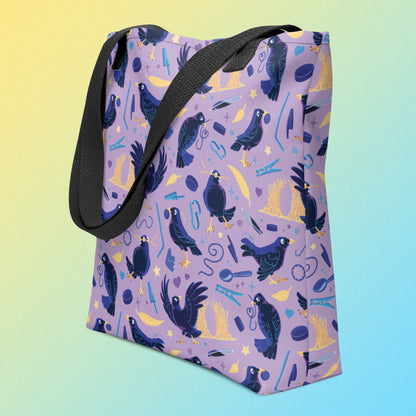 Tote bag with black handles and a purple/blue/yellow satin bowerbird pattern on an angle on a yellow and blue gradient background