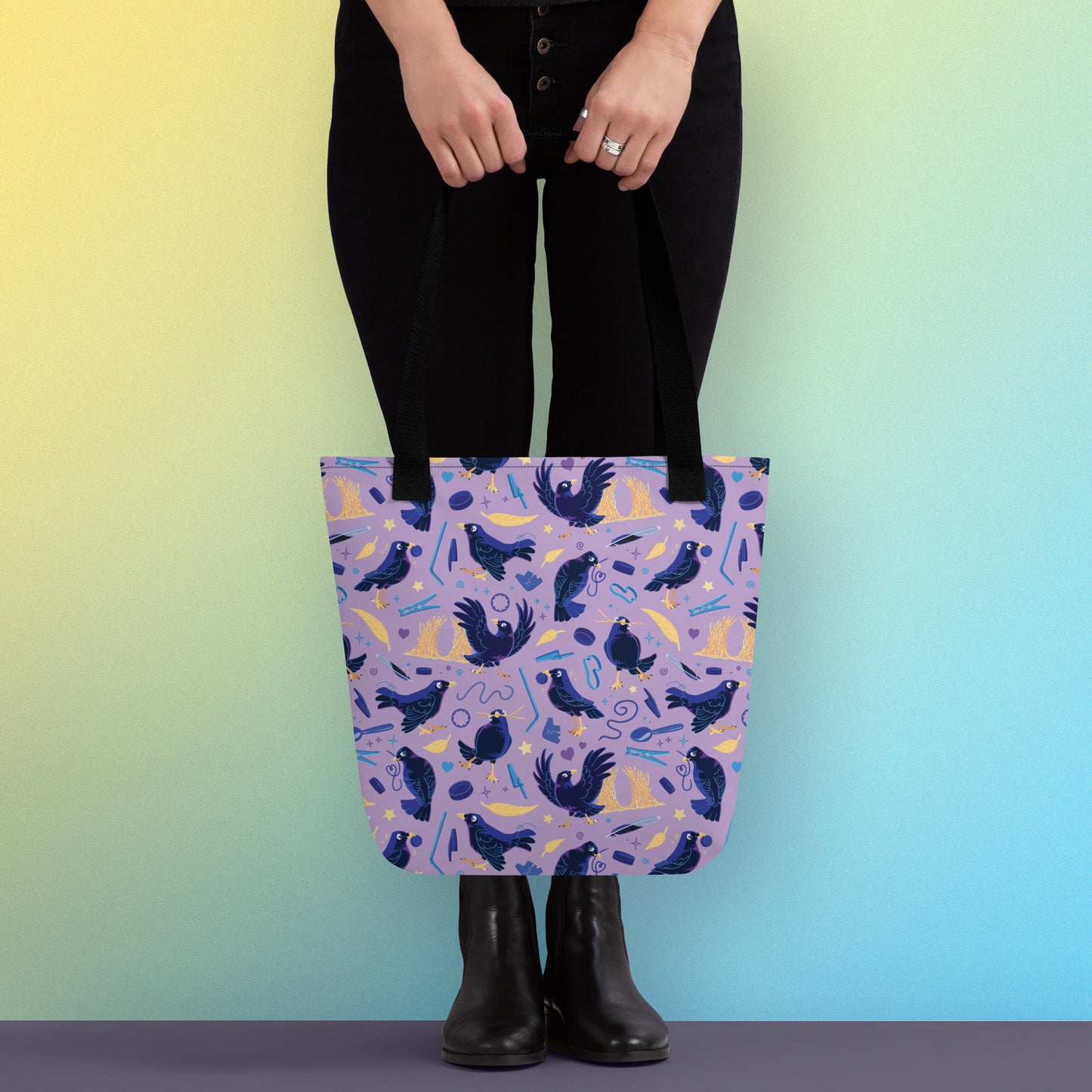 Person holding a tote bag with black handles and a purple/blue/yellow satin bowerbird pattern on a yellow and blue gradient background