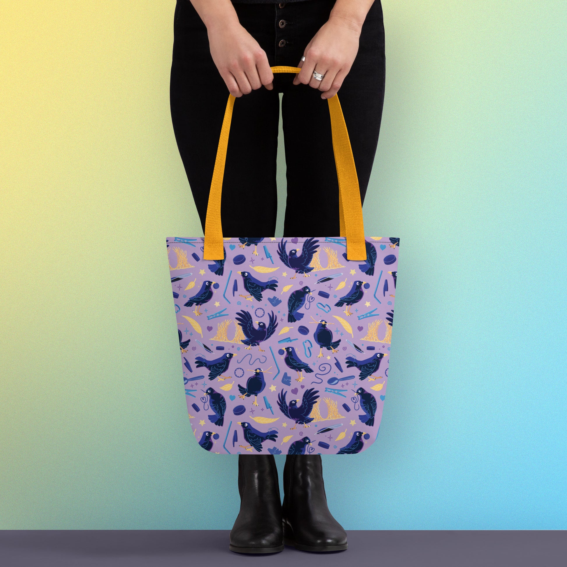 Person holding a tote bag with yellow handles and a purple/blue/yellow satin bowerbird pattern on a yellow and blue gradient background