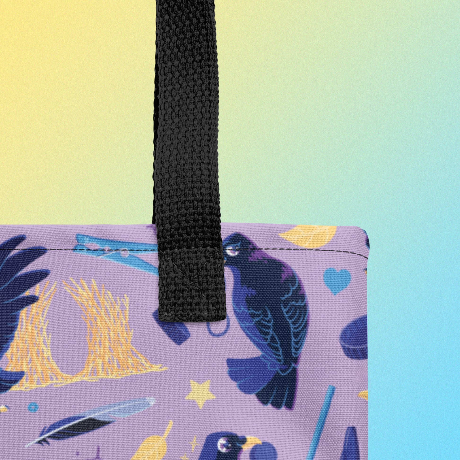 Close up of a tote bag with black handles and a purple/blue/yellow satin bowerbird pattern on a yellow and blue gradient background